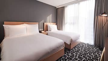 A hotel room with two beds, a modern design, a geometric patterned carpet, and a large window with curtains.