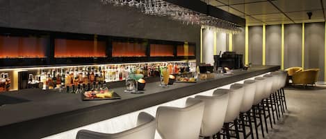 Zona de bar moderna con una barra larga, diversas opciones de asientos y una variedad de botellas y vasos.