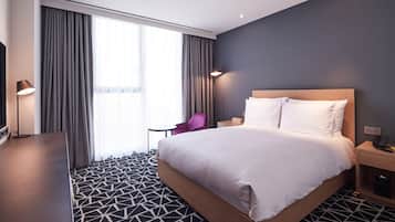 A modern hotel room with a large bed, a desk, a chair, and a TV.