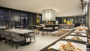 Een moderne eetruimte met meerdere tafels en stoelen, een centraal bedieningsstation en uitzicht op de skyline door grote ramen.