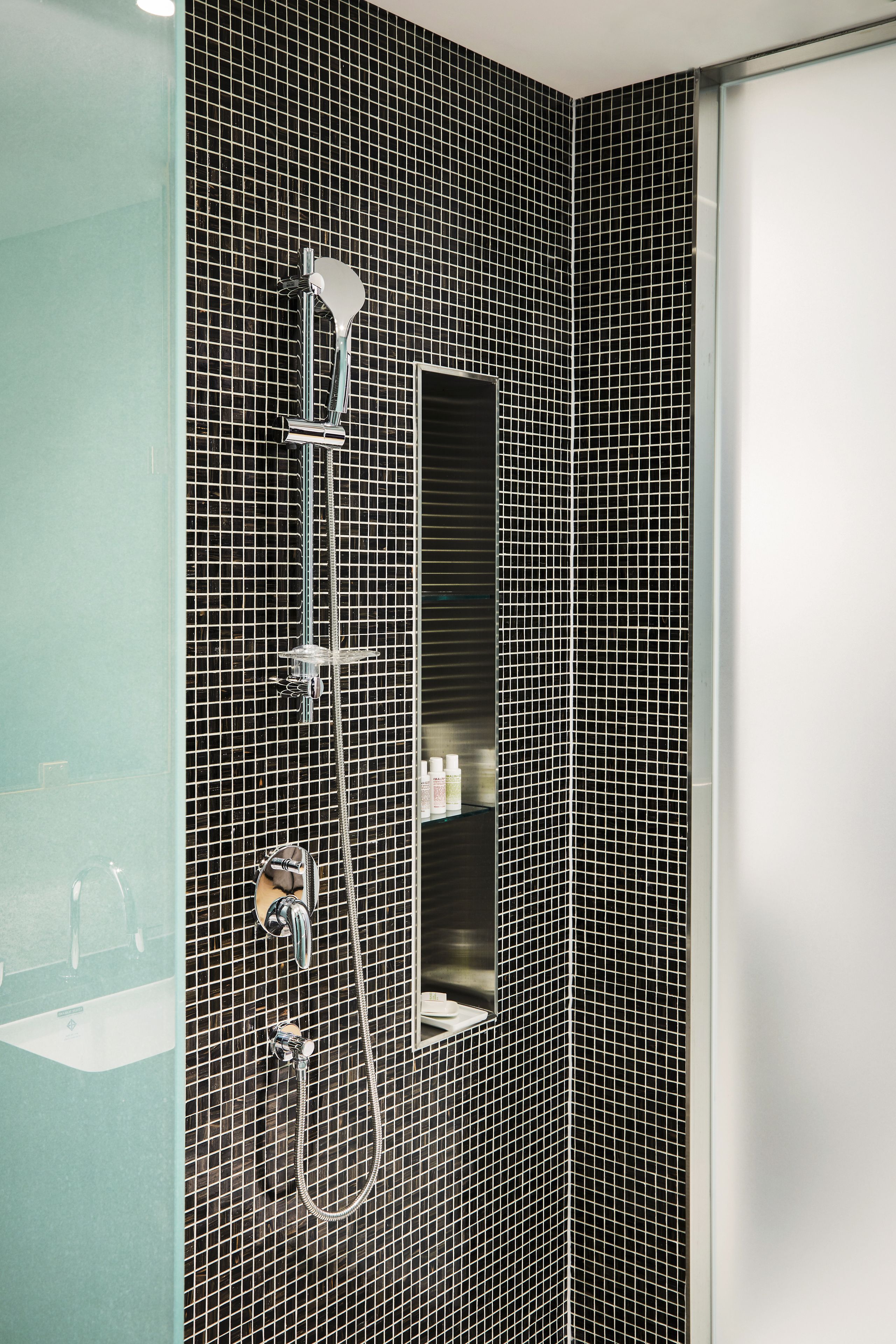 Un baño con paredes de azulejos blancos y negros, una ducha con cabezal de ducha de mano y un espejo con marco de vidrio.