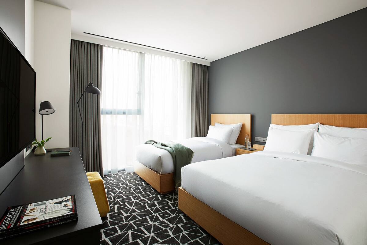 Une chambre d’hôtel avec un grand lit, un lit plus petit, un bureau avec une lampe et une télévision.