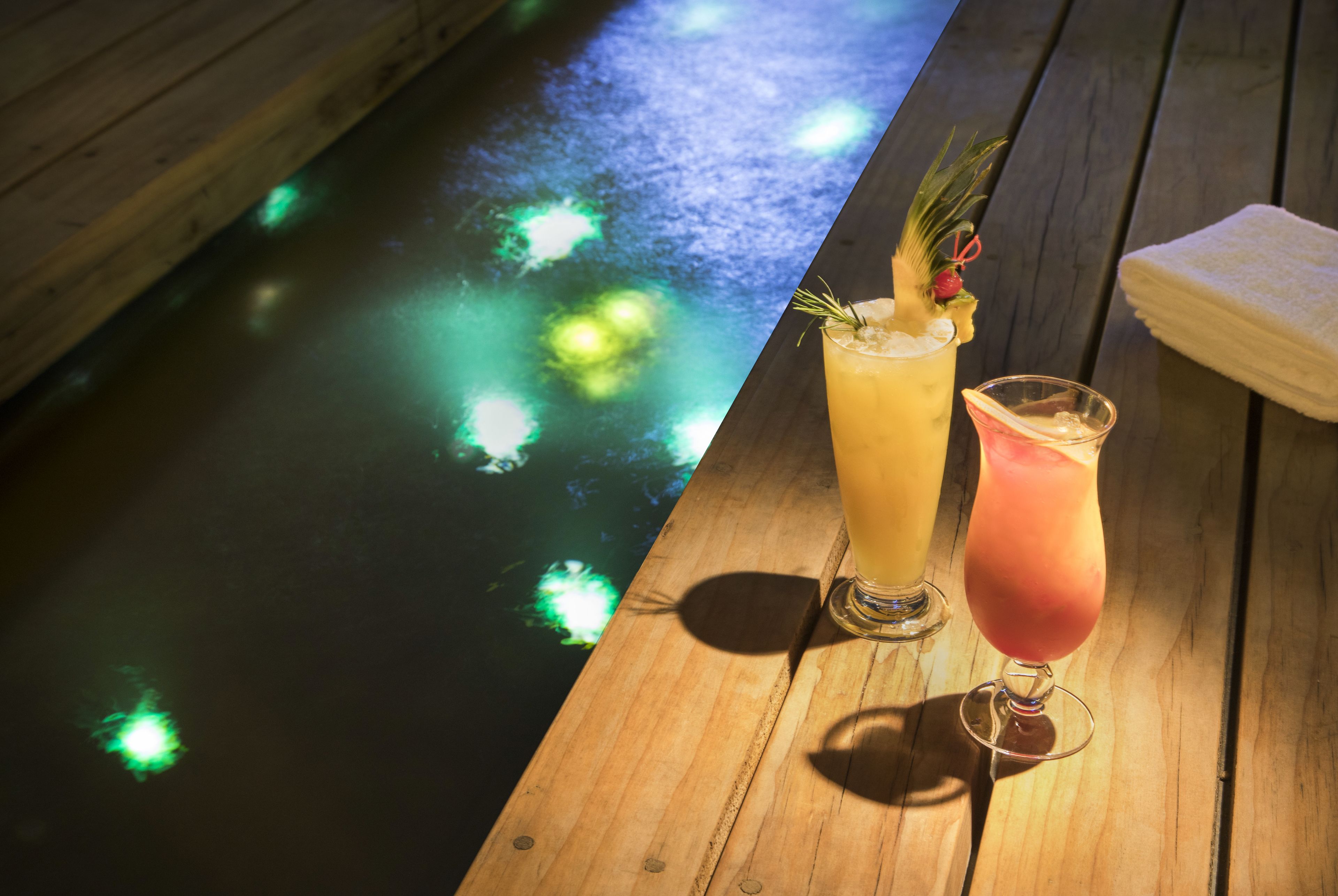 Two drinks on a wooden table with a pool in the background.