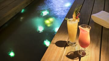 Two drinks on a wooden table with a pool in the background.