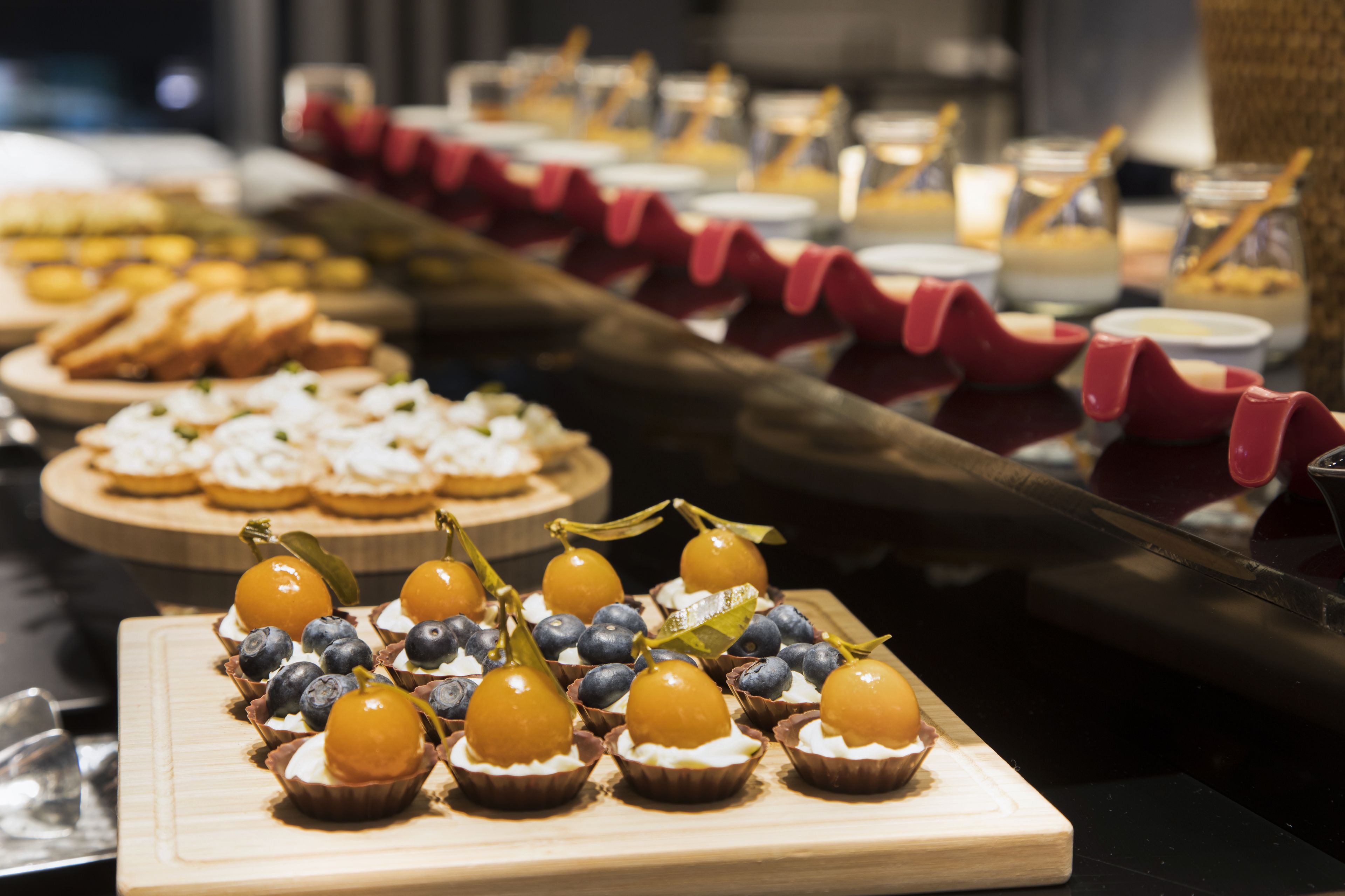 A buffet with various desserts including cupcakes with blueberries and a pear, and other pastries.