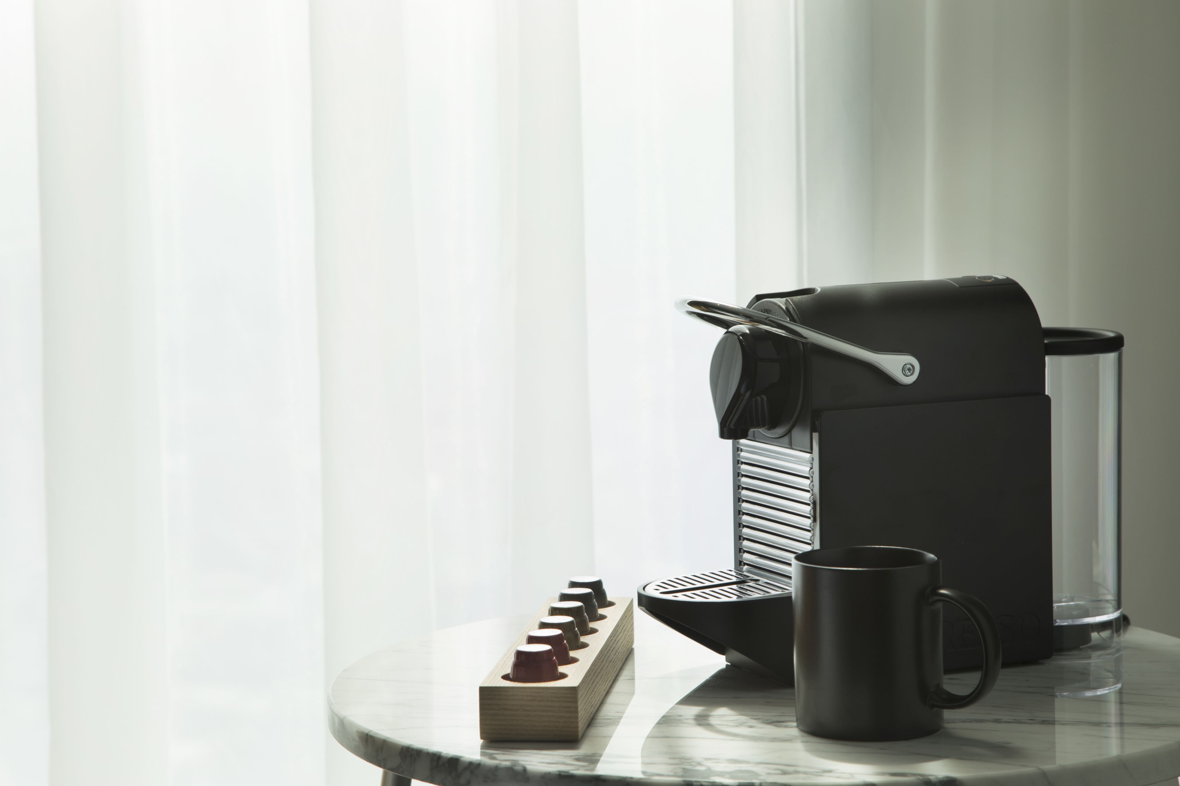Una cafetera sobre una mesa de mármol con una jarra de café y una taza.