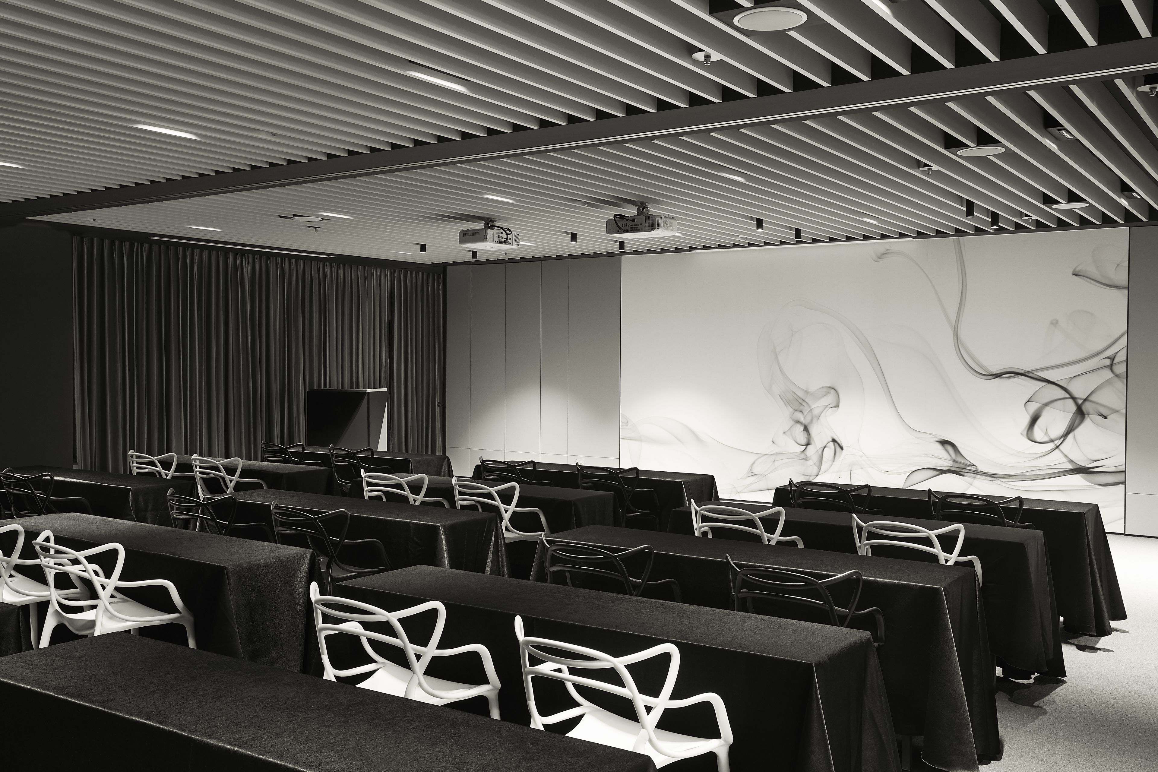 A conference room with rows of tables and chairs, a large screen, and a modern ceiling design.