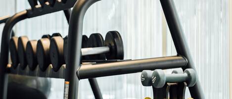 A gym with a rack of dumbbells, a towel, and a water bottle on the floor.