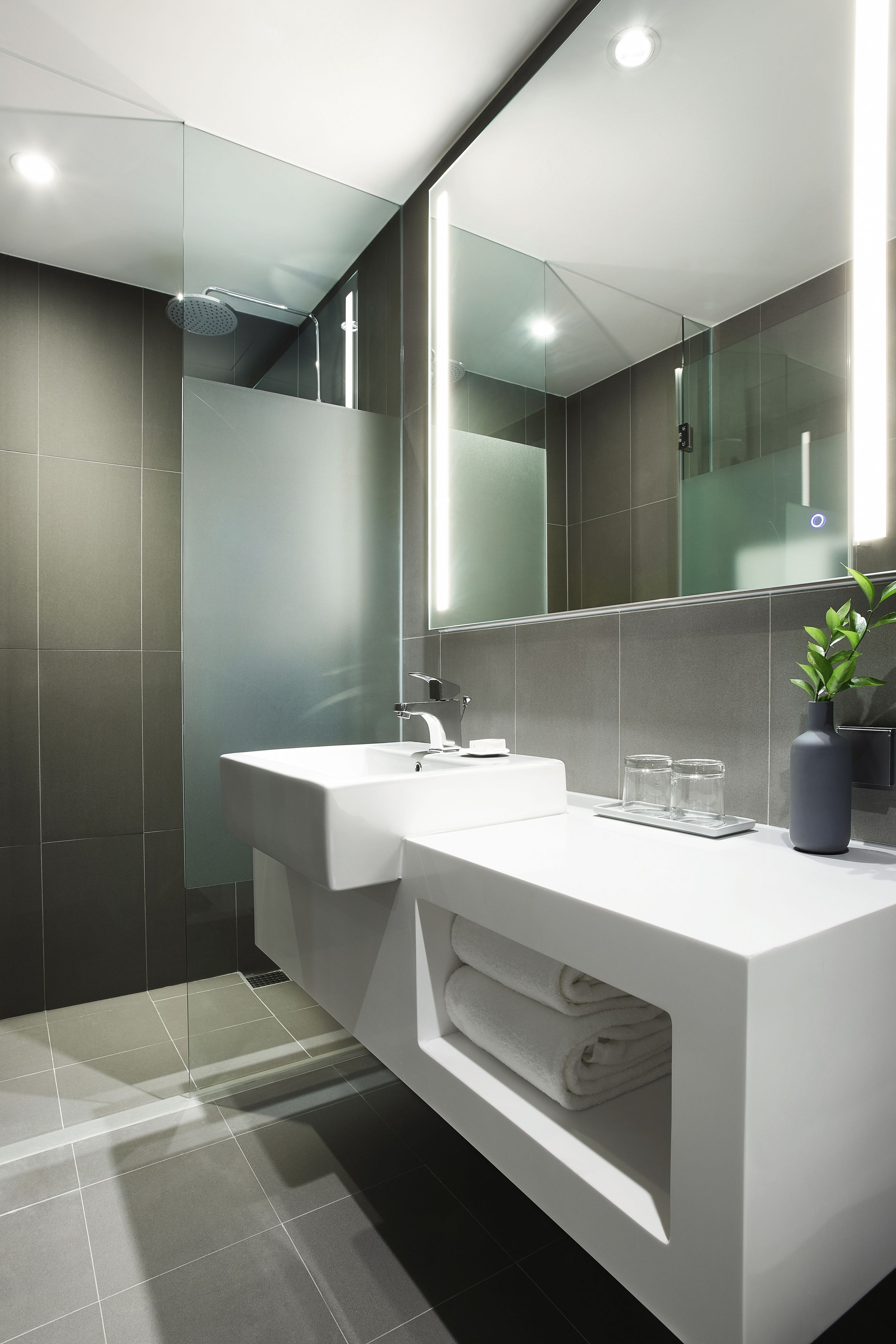 A modern bathroom with a large mirror, a white sink, and a glass shower enclosure.