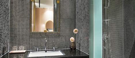A bathroom with black and white tiled walls, a sink with a mirror above it, and a shower area.