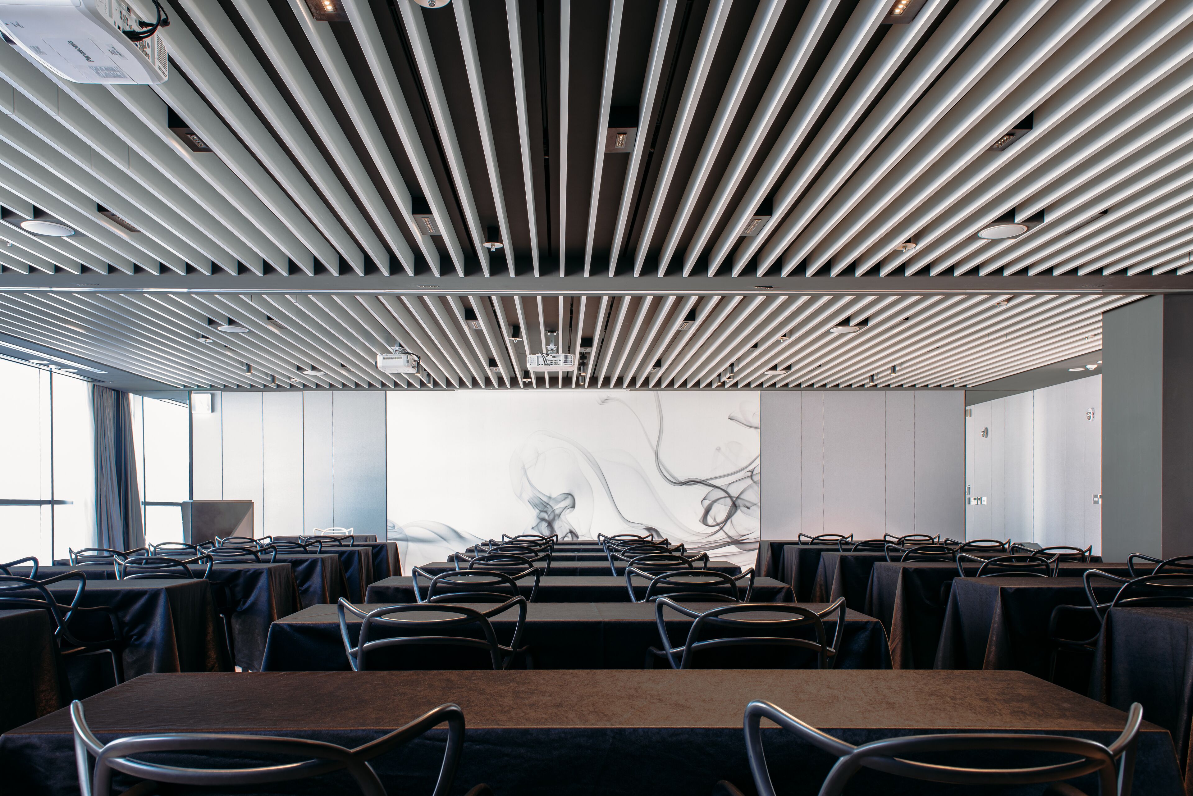 A conference room with a modern ceiling design, multiple tables, and chairs arranged for meetings.