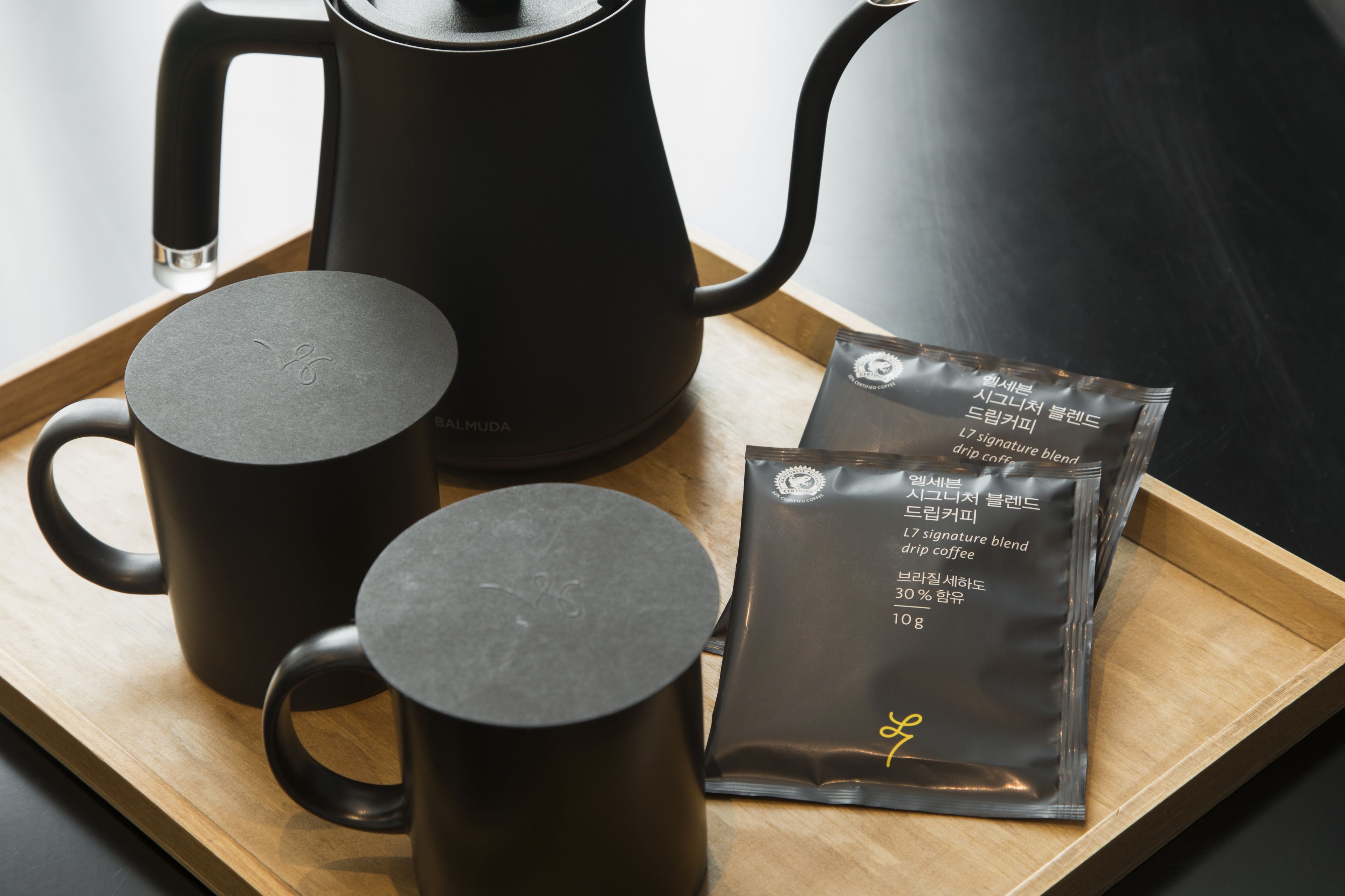 A tray with a black coffee maker, two black mugs, and a packet of coffee.