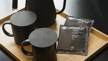 A tray with a black coffee maker, two black mugs, and a packet of coffee.