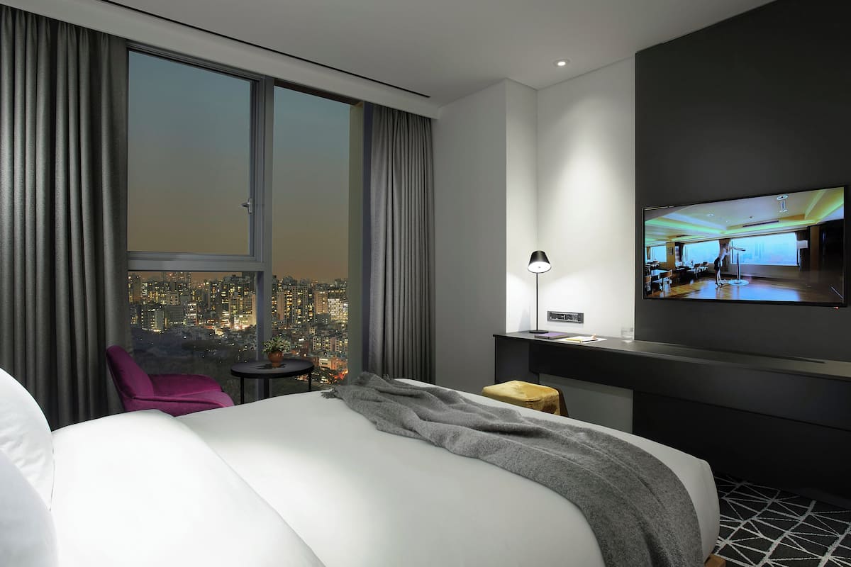 A modern hotel room with a large bed, a desk, a chair, and a TV mounted on the wall.