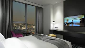A modern hotel room with a large bed, a desk, a chair, and a TV mounted on the wall.