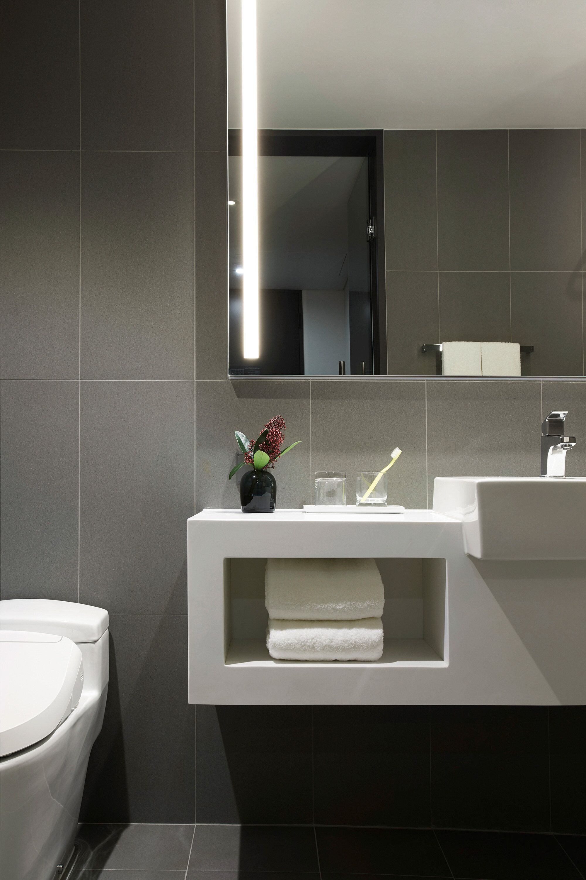 Un baño moderno con un inodoro blanco, un lavabo blanco y un espejo sobre el lavabo.