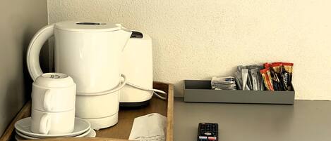 A coffee maker, a remote control, and a tray with a cup and saucer on a table.