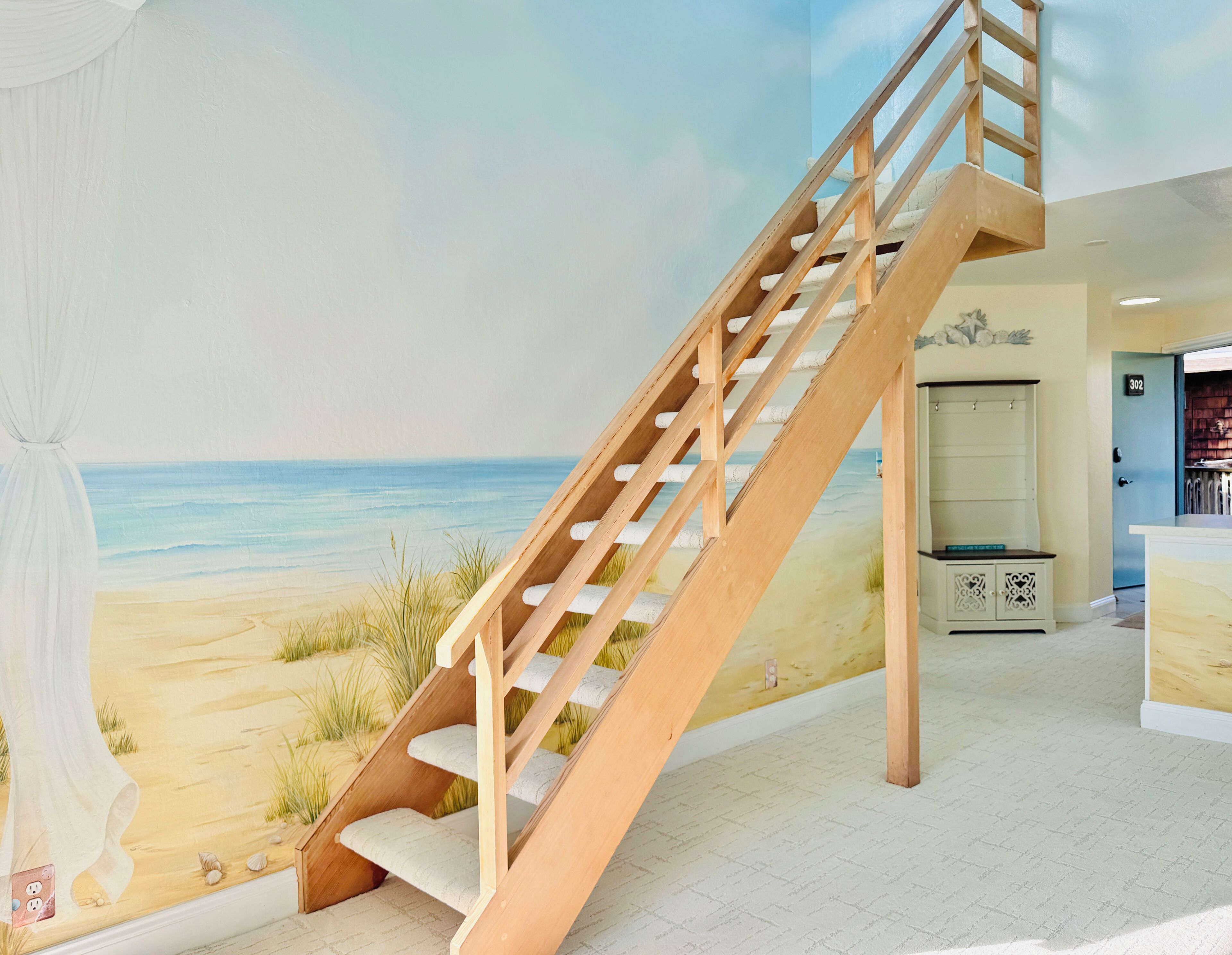 Een houten trap die leidt naar een muurschildering met een strandthema, een wit kastje en een deur met nummer 302.