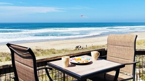 Mesa y sillas en la playa, un plato de comida y dos tazas, con vistas al océano.