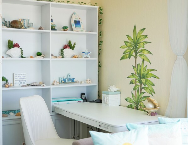 A room with a white desk, shelves with decorative items, a large plant, and a chair. - Epic 180° Ocean Views: Monterey to Santa Cruz + Stunning Mural Interior (Watsonville)