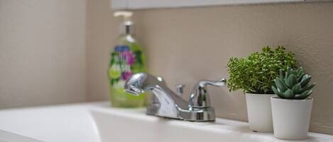 A bathroom sink with a modern faucet, a bottle of liquid soap, and two small potted plants.