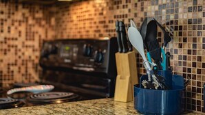 A kitchen with a tiled backsplash, a granite countertop, and a blue utensil holder with various kitchen tools.