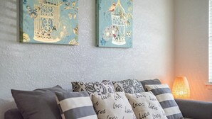 A living room with a grey sofa, patterned cushions, and two wall art pieces depicting birdcages.