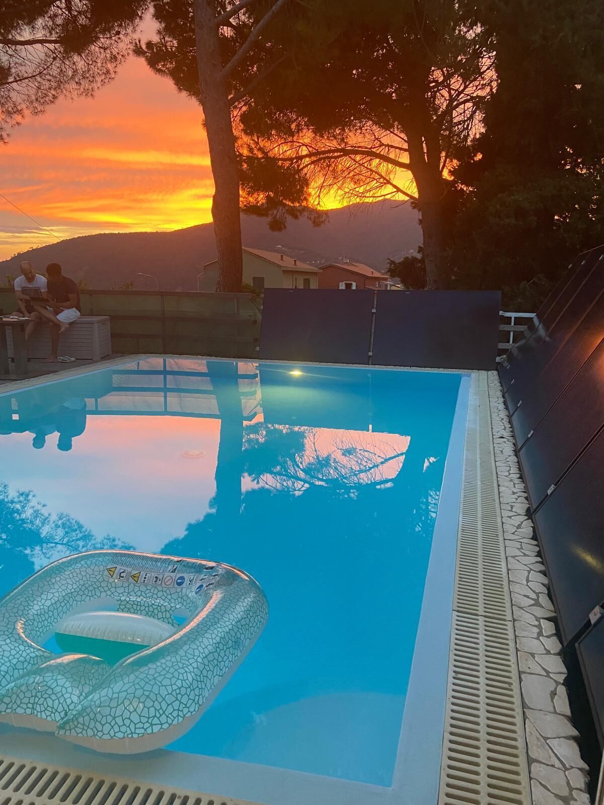 A swimming pool with a hot tub, surrounded by trees and a sunset view.