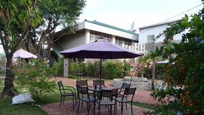 Un patio al aire libre con una mesa y sillas de ladrillo, rodeado de follaje y un edificio al fondo.