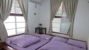 Un dormitorio con una cama de madera, ropa de cama púrpura y dos ventanas con cortinas.
