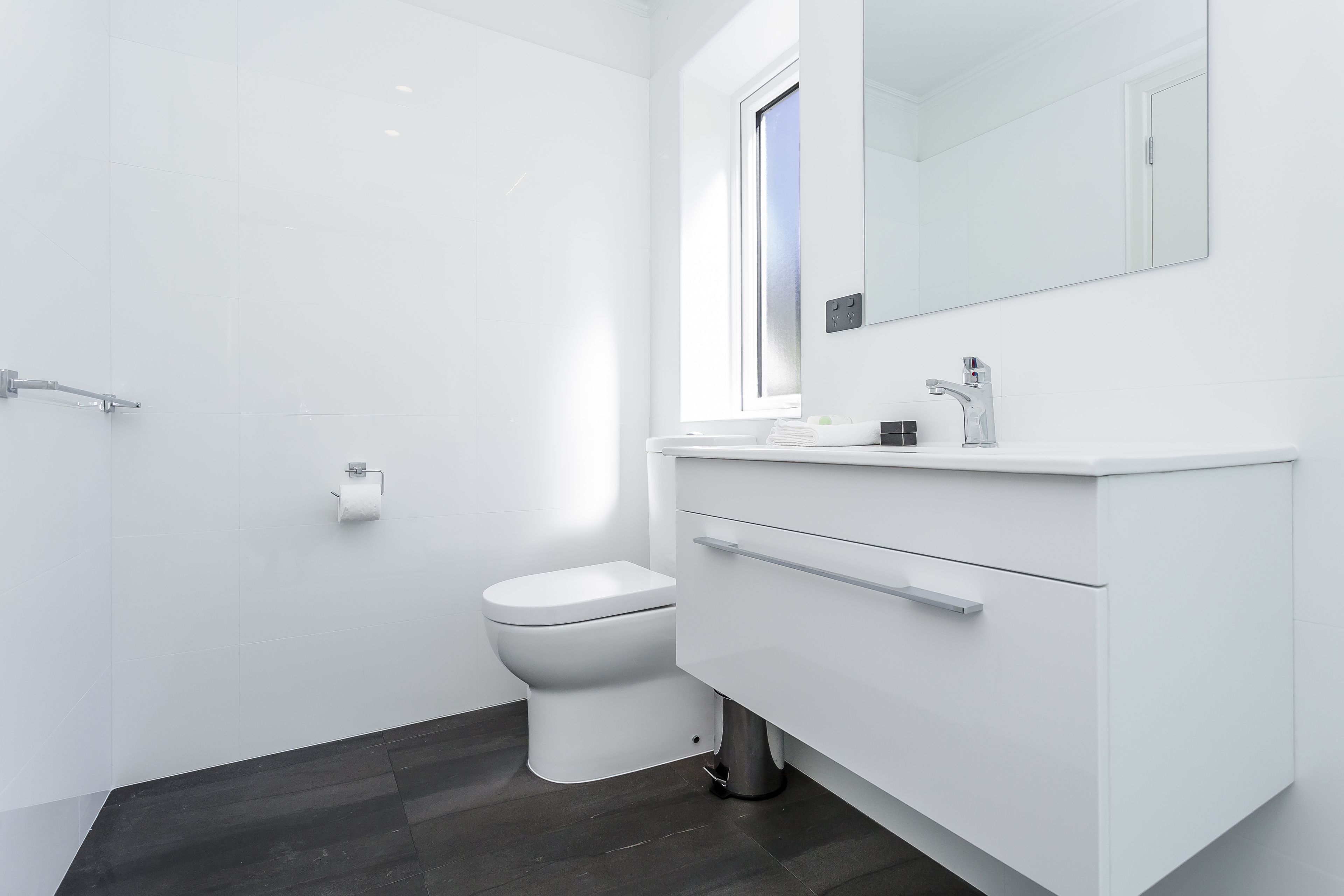 Une salle de bain moderne équipée de toilettes, d’un meuble-lavabo avec miroir et d’une fenêtre.