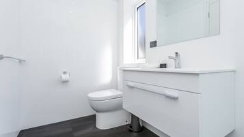 Une salle de bain moderne équipée de toilettes, d’un meuble-lavabo avec miroir et d’une fenêtre.