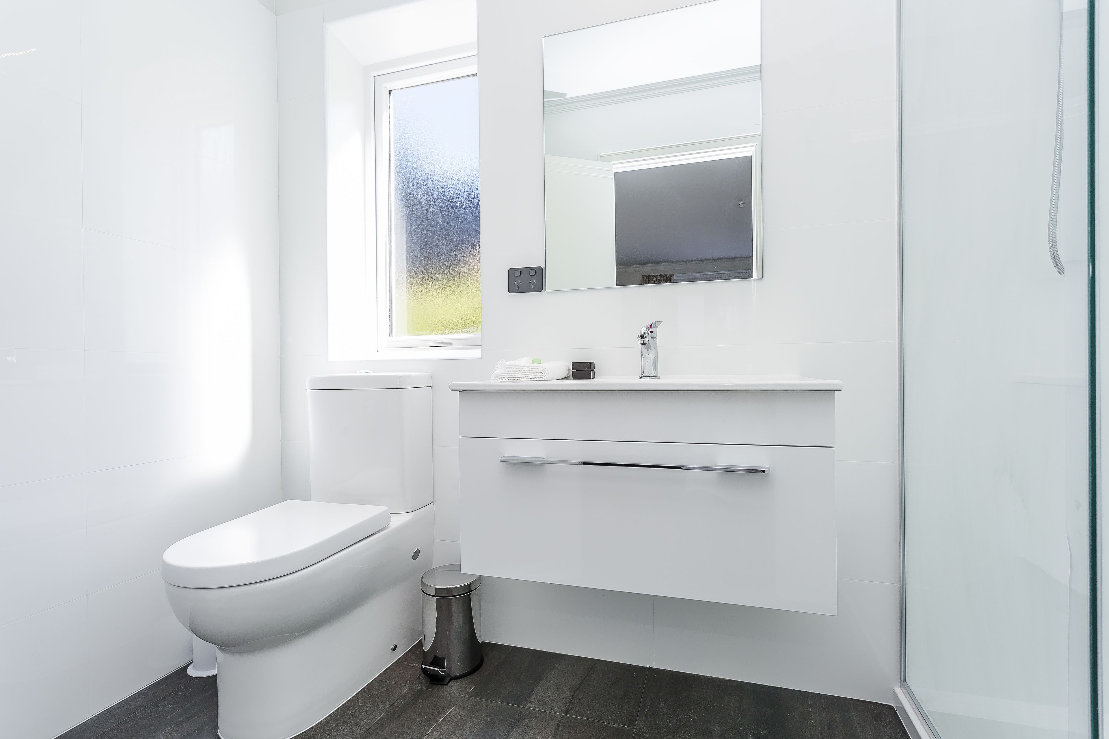 A modern bathroom with a toilet, a sink, a mirror, and a window.
