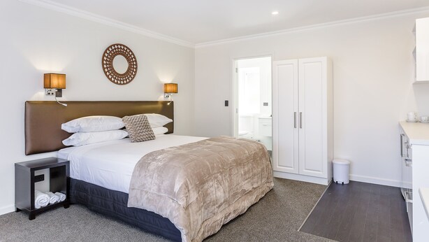 A modern hotel room with a large bed, bedside lamps, a round mirror, and a wardrobe. - Superior Dunedin Apartments (Dunedin)