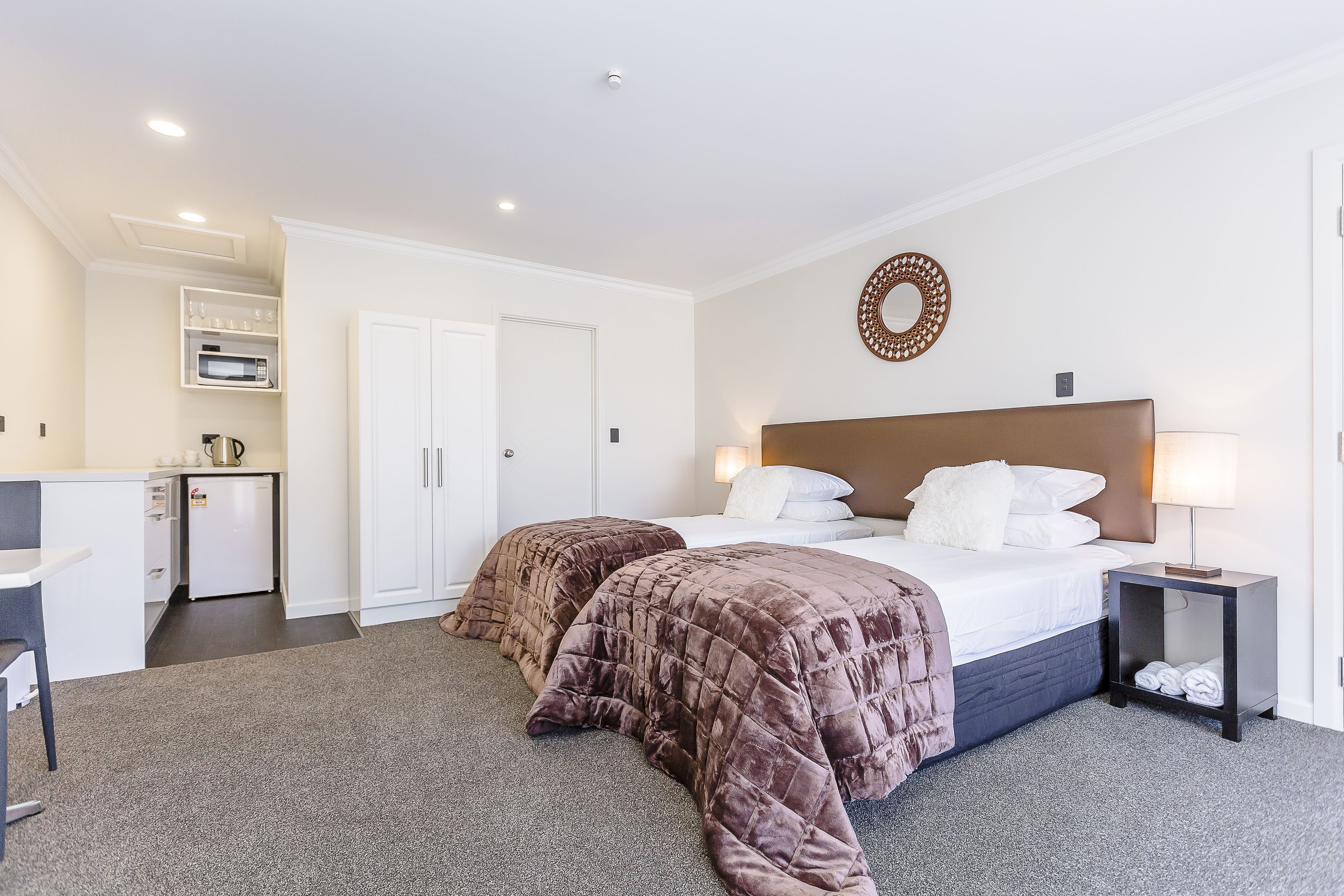 A hotel room with a bed, bedside table, and a small desk with a chair.