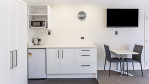 A compact kitchenette with a microwave, coffee maker, and refrigerator. A wall-mounted clock and a flat-screen TV are also visible. - Superior Dunedin Apartments (Dunedin)