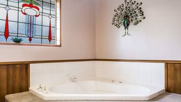 A bathroom with a freestanding bathtub, a decorative stained glass window, and a wall-mounted peacock sculpture.