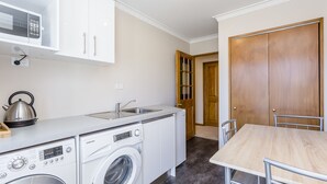 A compact kitchen with a washing machine, a microwave, and a sink. - Superior Dunedin Apartments (Dunedin)