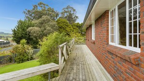 A wooden deck leading to a brick house with large windows and a view of a lush garden and trees. - Superior Dunedin Apartments (Dunedin)