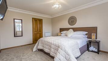 A bedroom with a large bed, a bedside table with a lamp, a mirror on the wall, and a door.