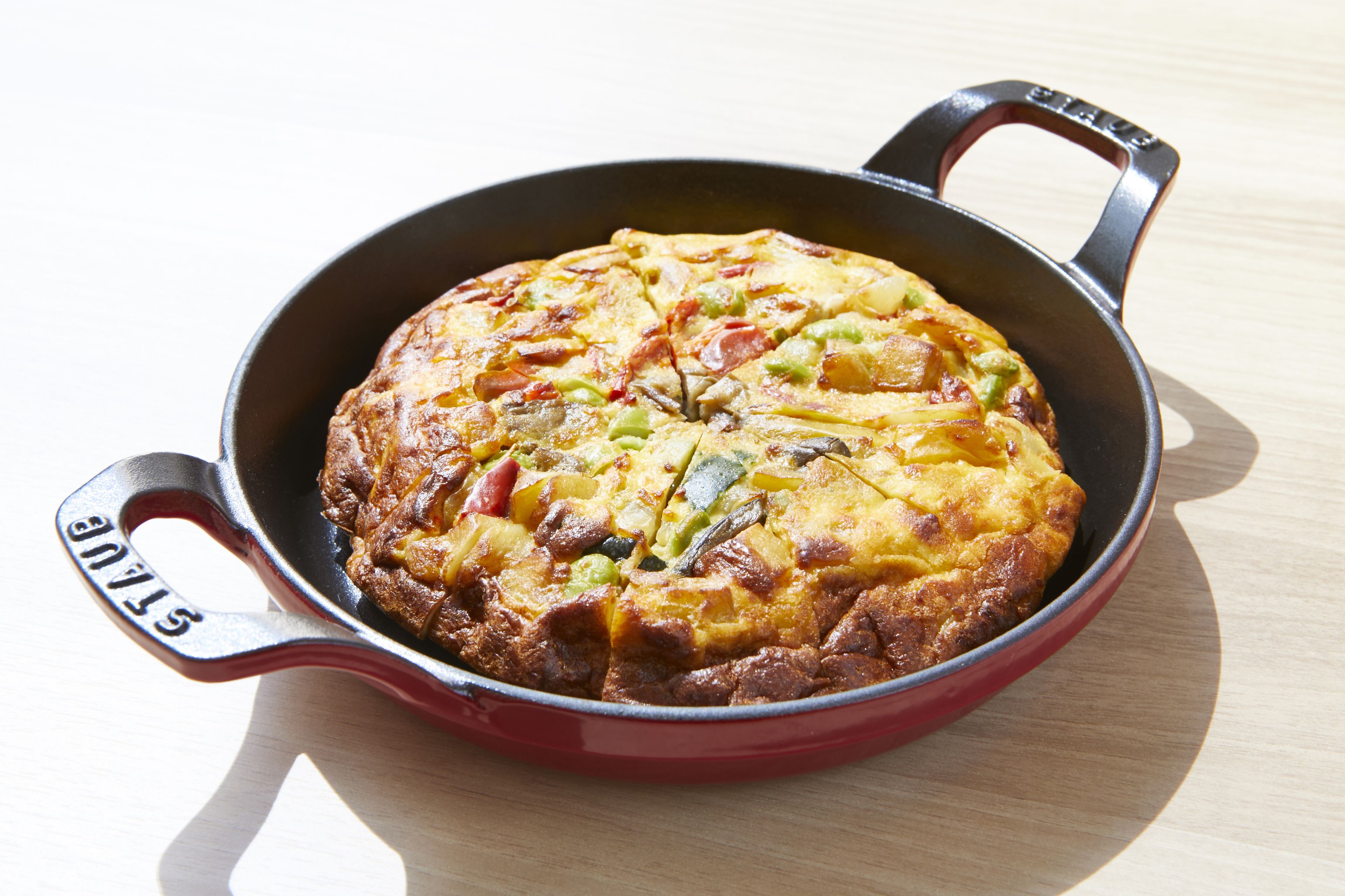 A skillet with a frittata containing vegetables and meat.