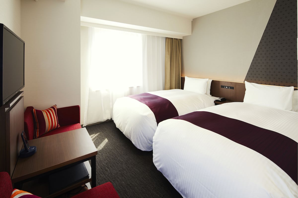 Habitación de hotel con dos camas, televisión, escritorio y ventana con cortinas.