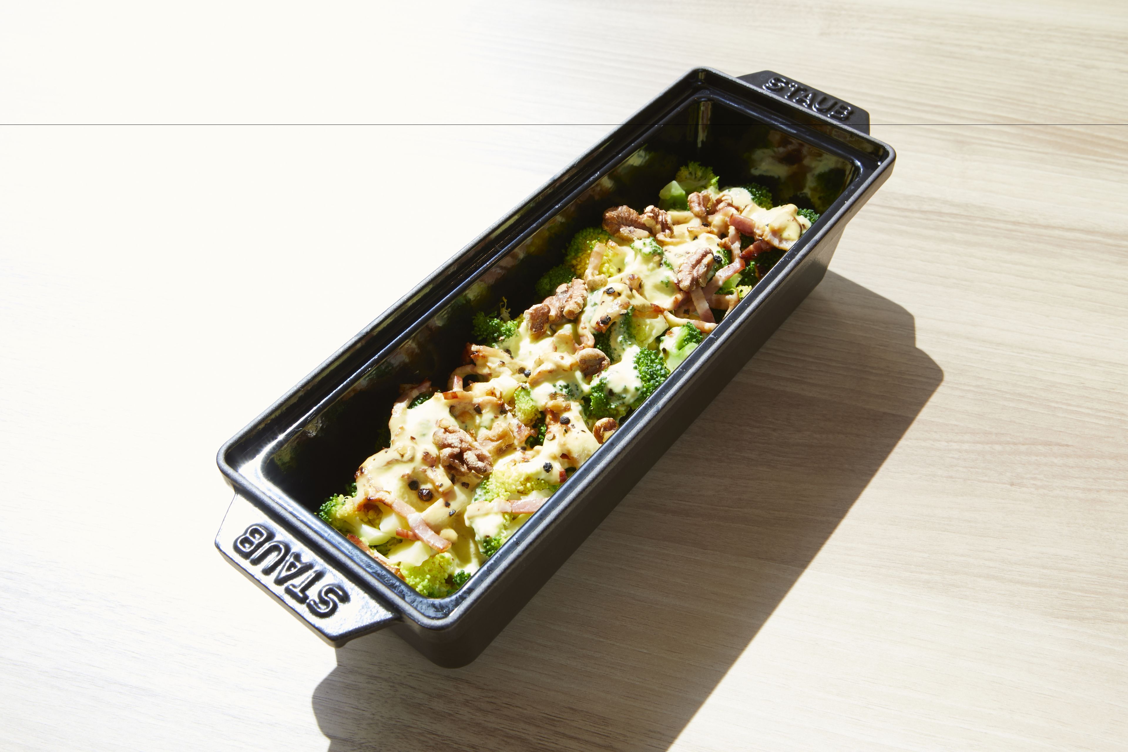 A rectangular black tray with the word "STAX" on it, containing a dish with broccoli and noodles.
