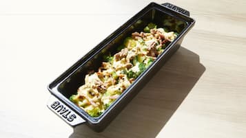 A rectangular black tray with the word "STAX" on it, containing a dish with broccoli and noodles.