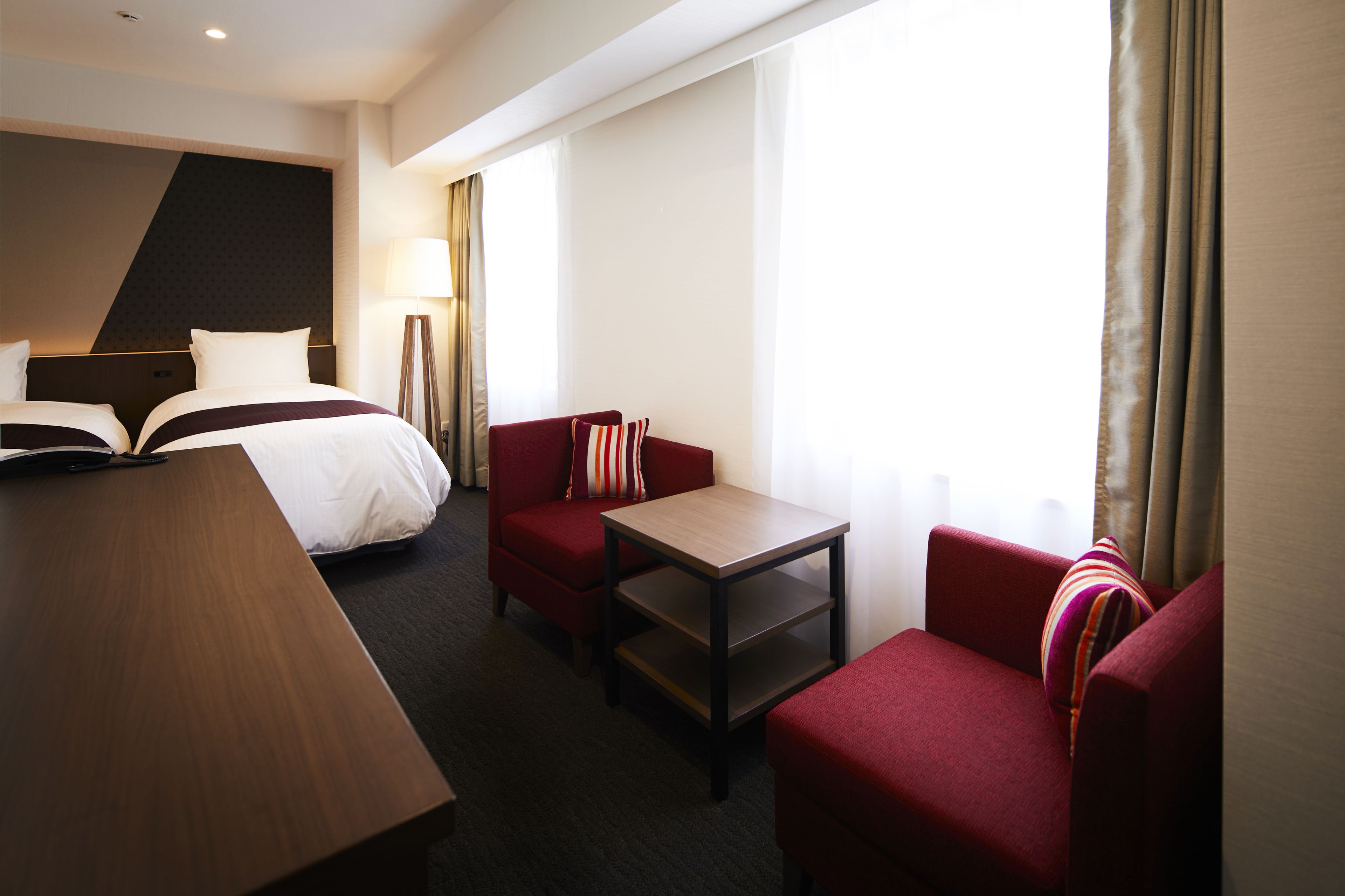 A hotel room with a bed, a desk, a chair, and a sofa.