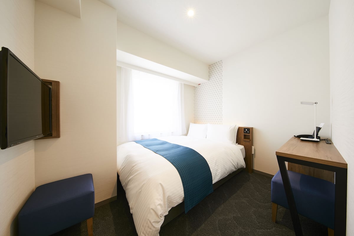 Habitación de hotel con cama, mesita de noche, escritorio y televisor.