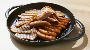 A cast iron skillet with grilled meat and sausages.