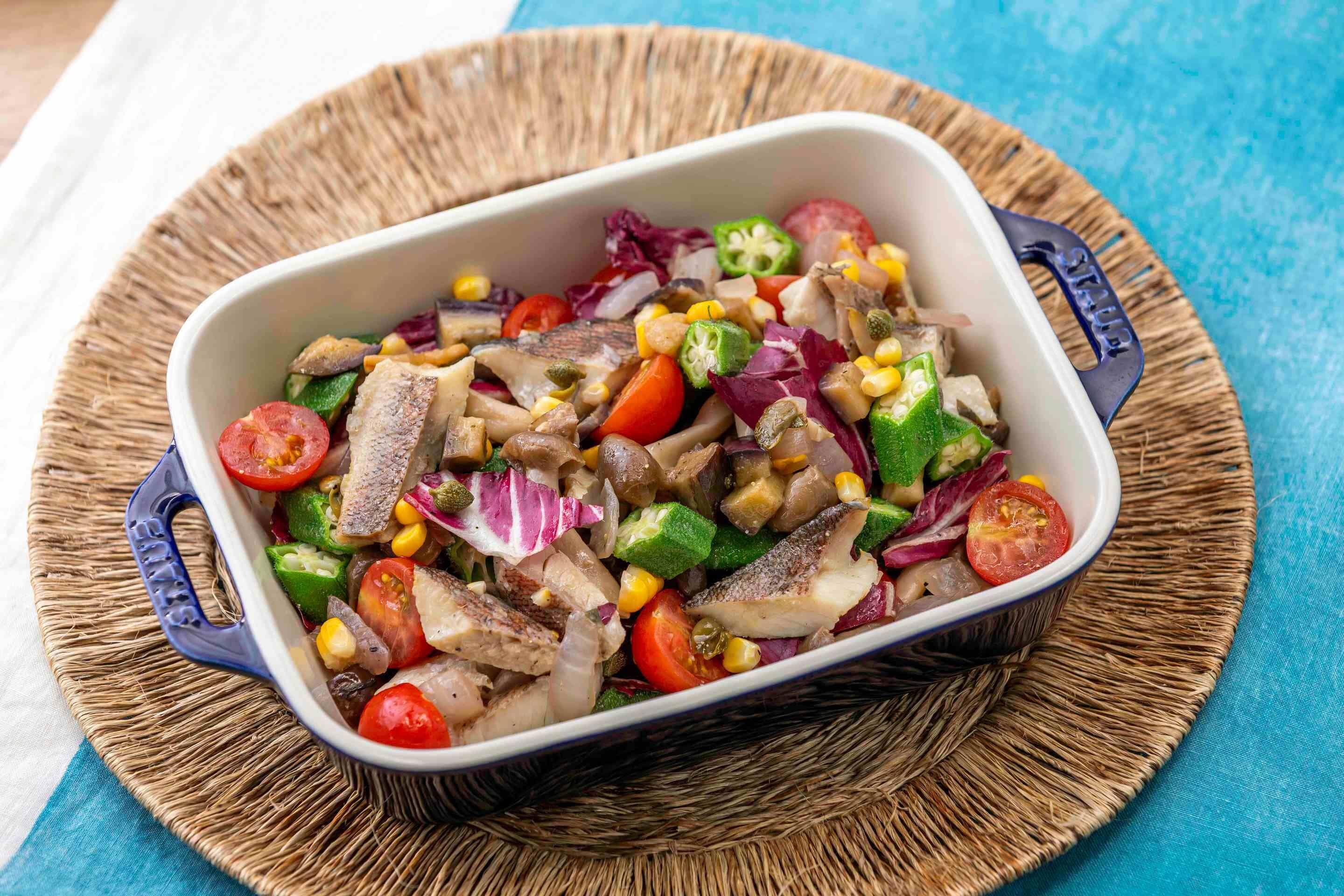 Un piatto rettangolare con manico, contenente un'insalata colorata con diverse verdure e pesce.