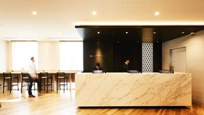 Un comptoir d’accueil d’hôtel avec un plateau en marbre, un séparateur noir et un espace d’accueil doté d’un plancher en bois.