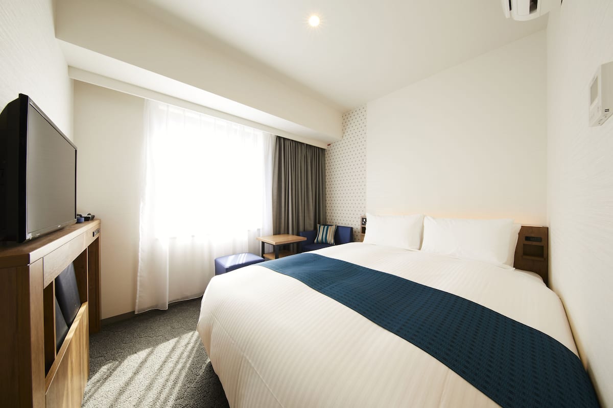 Una habitación de hotel con una cama grande, un escritorio, un televisor y una ventana con cortinas.